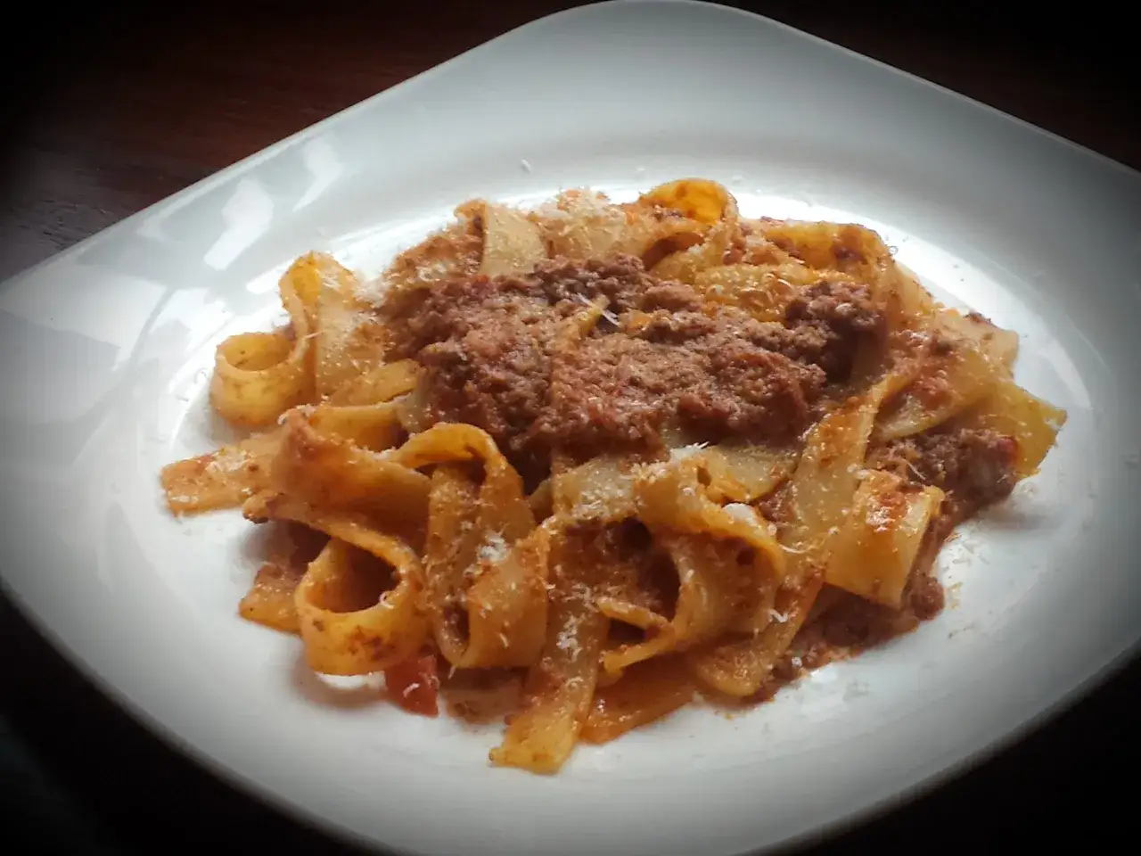 Pappardelle ragu z parmezanem na białym talerzu.