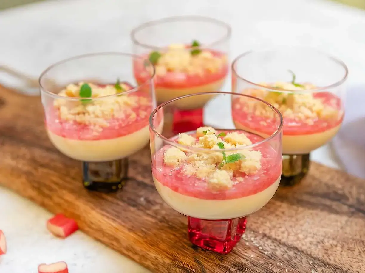 Fyra glas med krämig pannacotta med rabarberkompott och smuldeg. Garnerad med mynta. En härlig sommardessert.