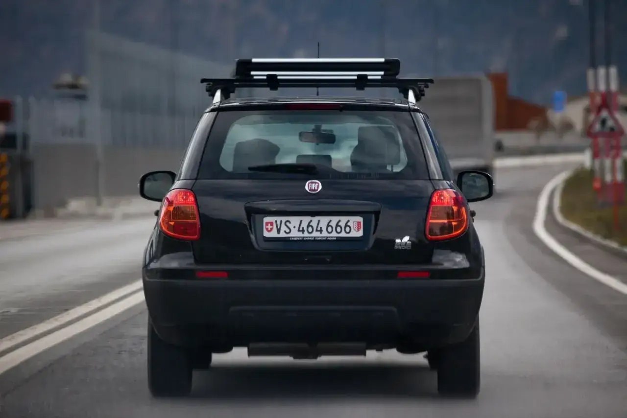 Czarny Fiat z bagażnikiem dachowym na drodze w Szwajcarii. Uważaj na mandaty w Szwajcarii, bo są wysokie!