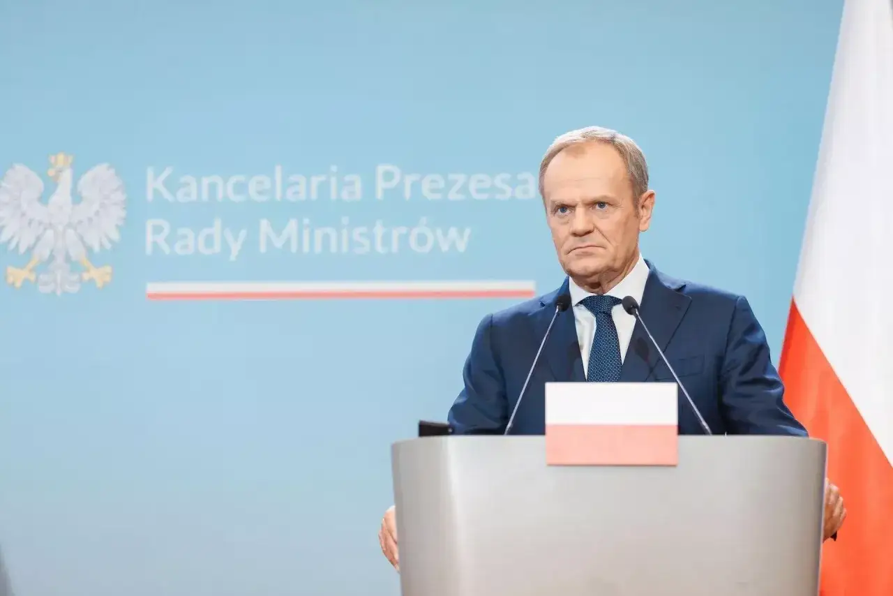 Donald Tusk przemawia na tle godła Polski i napisu