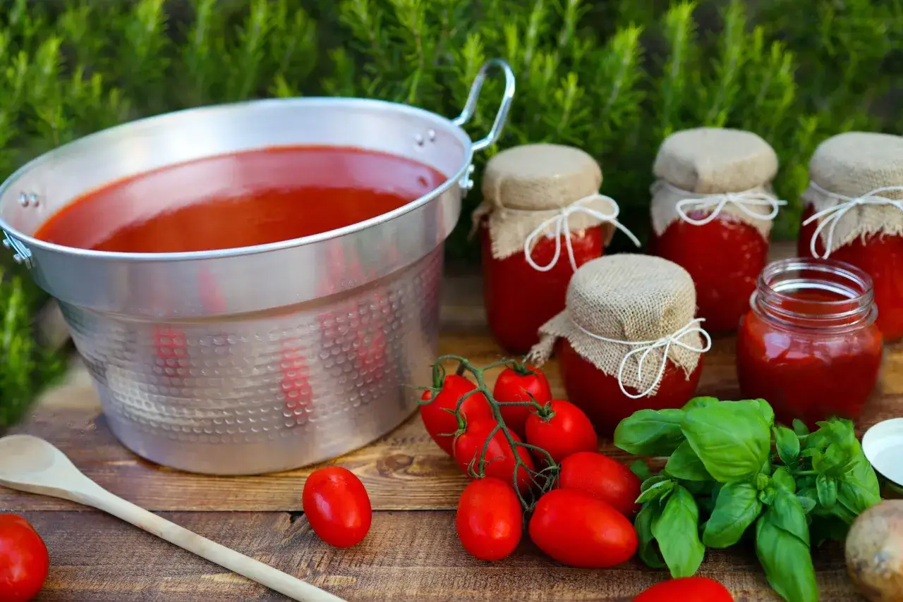Un grande pentolone di pomodoro pronto per diventare ketchup fatto in casa, con vasetti già pronti, pomodori freschi e basilico.
