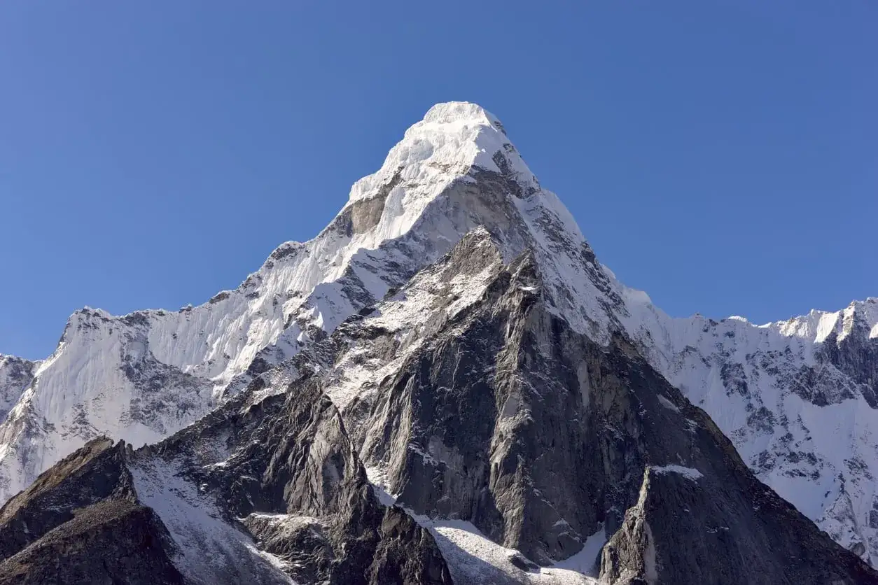 Majestatyczny, ośnieżony szczyt Amadablam, jeden z największych szczyt&oacute;w na świecie, g&oacute;ruje nad skalistymi zboczami w czystym, błękitnym niebie.