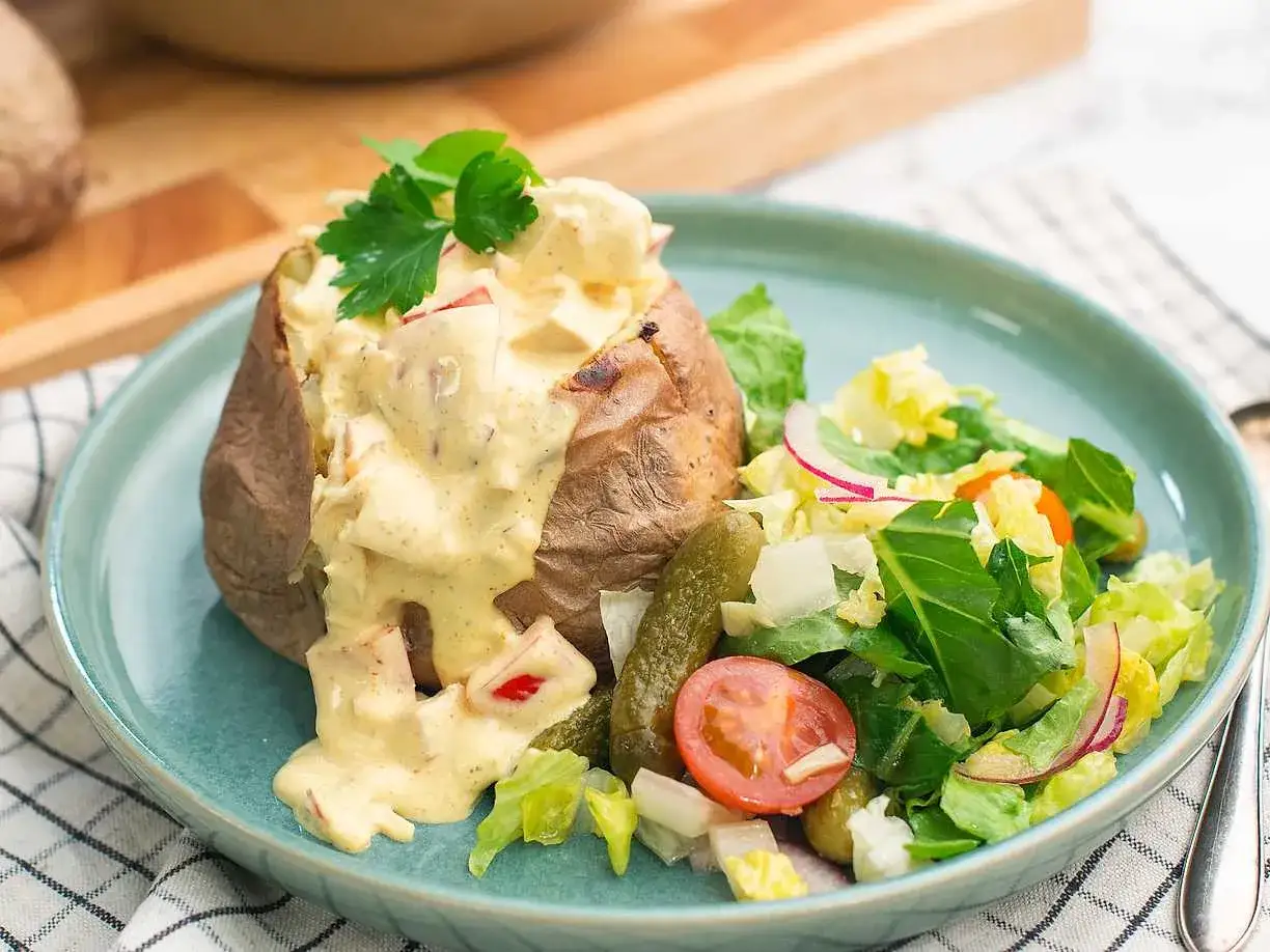 En saftig bakad potatis med en kr&auml;mig fyllning av ost och gr&ouml;nsaker, serverad med en fr&auml;sch sallad och saltgurka.
