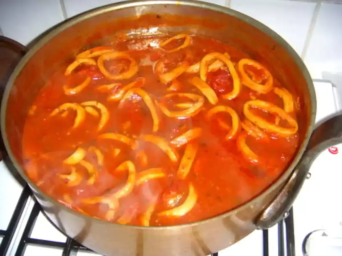 Un plat mijoté de calamars à l'armoricaine dans une cocotte en cuivre, la sauce tomate rouge vif enveloppe les anneaux de calamar.