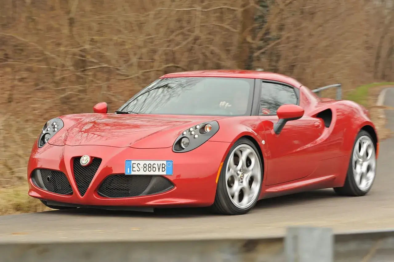 Czerwone Alfa Romeo 4C pędzi po krętej drodze, otoczone jesiennymi drzewami.