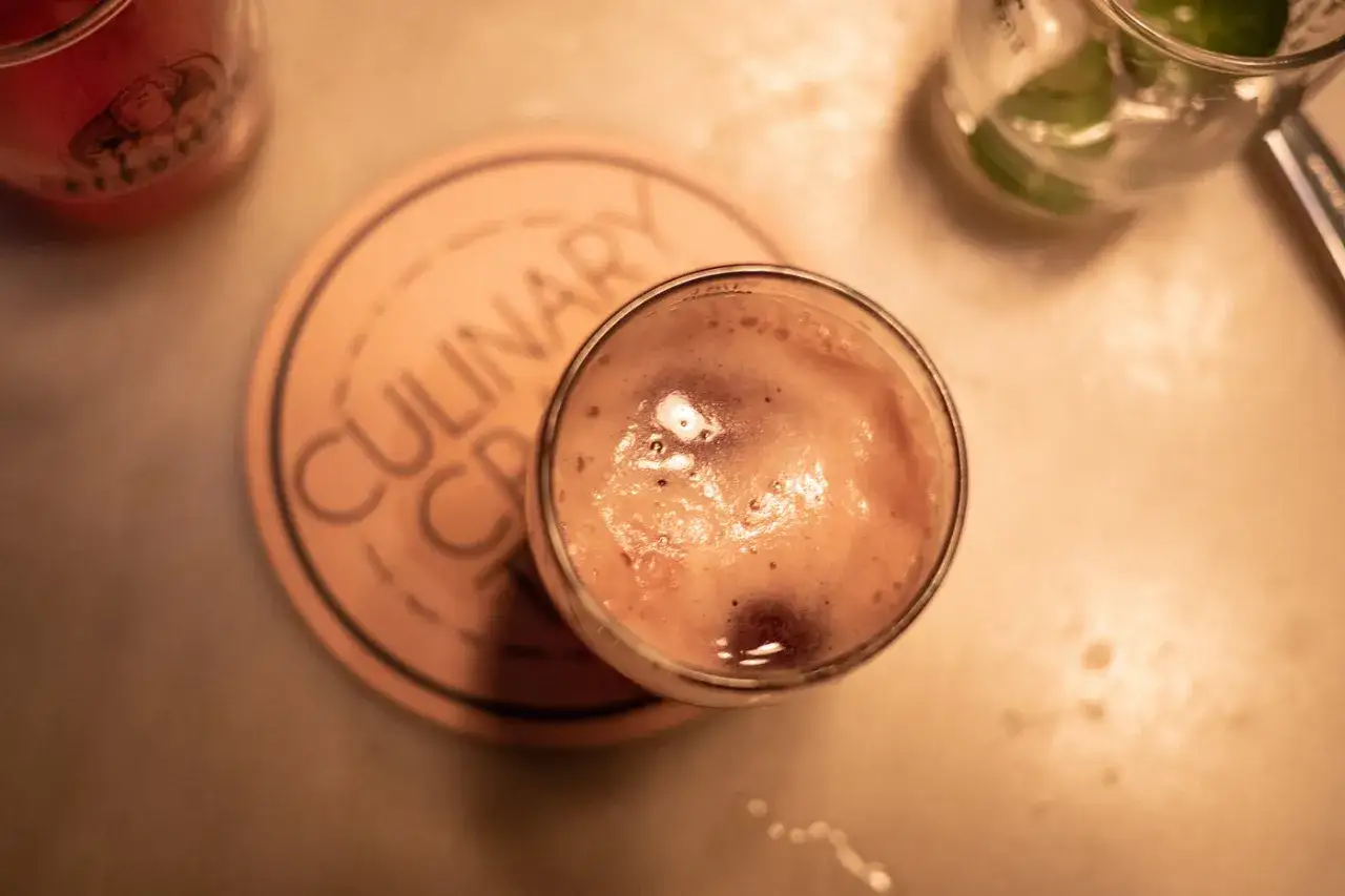 Ein schaumiger Bier-Cocktail steht auf einem Untersetzer. Daneben ein Glas mit Limette.