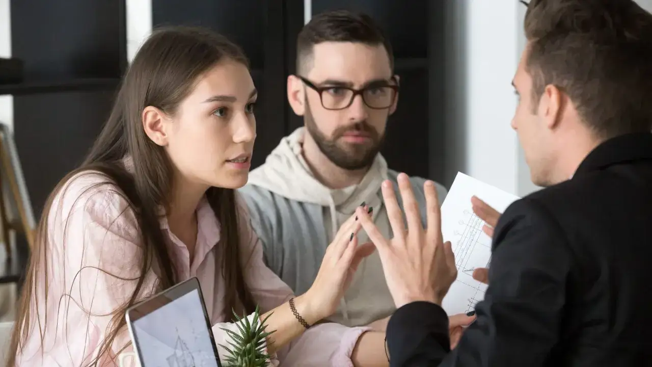 Ein Paar bespricht mit einem Berater eine Vorstandsbeschwerde Versicherung. Der Berater erklärt die Unterlagen.