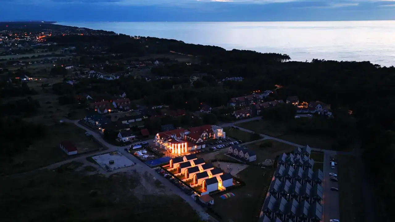 Ośrodek wczasowy Amber nocą, z oświetlonymi budynkami i morzem w tle.