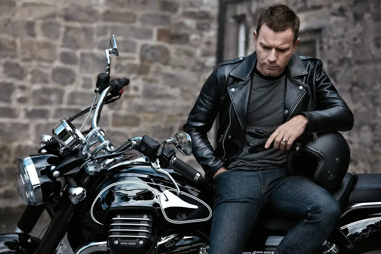 Ewan McGregor, con giacca di pelle e jeans, seduto su una scintillante Moto Guzzi.