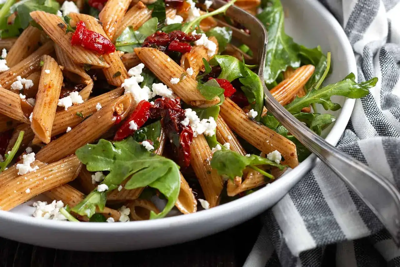 Herzhafter nudelsalat mit getrockneten tomaten, Rucola und Feta.