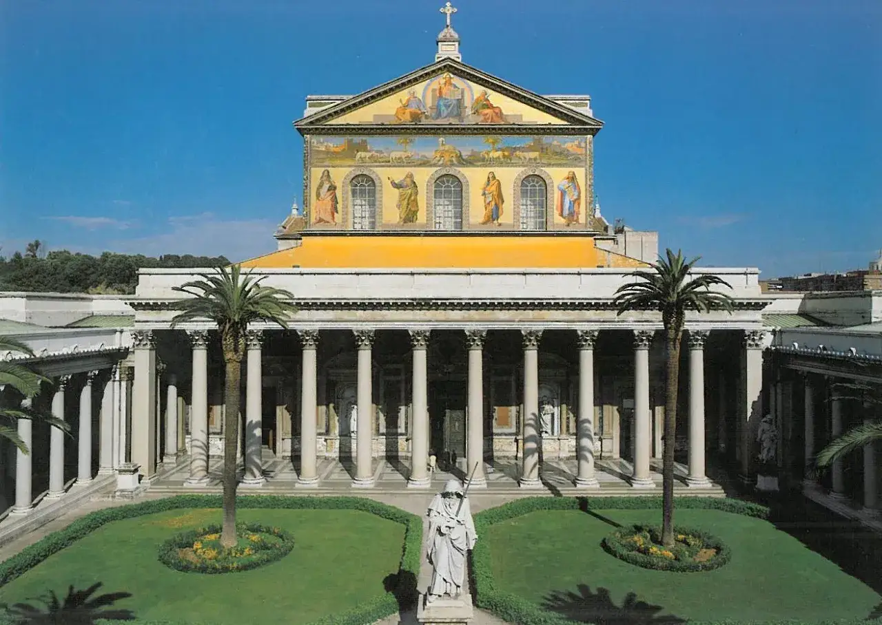 Cortile della cattedrale San Paolo a Roma, con statue, palme e un prato curato.