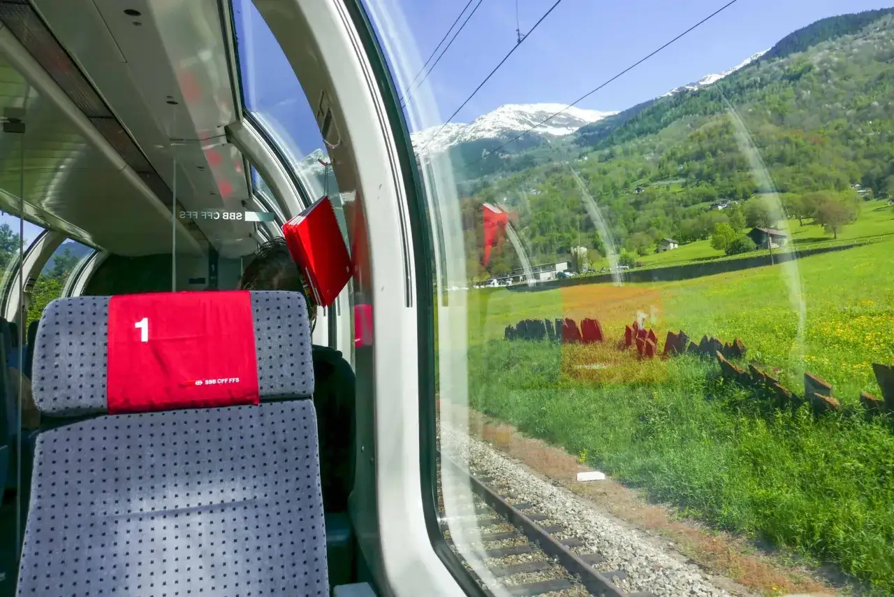 Scenic train journey from Tirano to Lugano, passing lush green valleys and snow-capped mountains.