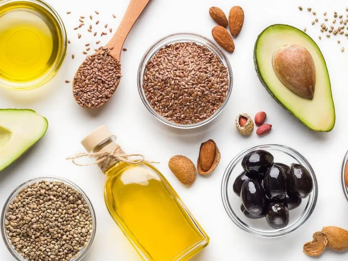 Huiles et graines : avocat, olives, amandes, lin, chanvre. Une bouteille d'huile dorée, riche en oméga 9, est entourée d'ingrédients sains.