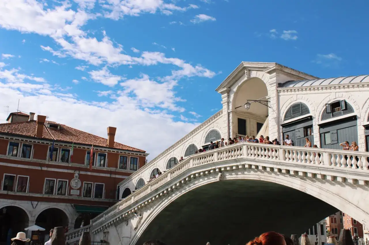 Una splendida giornata a Venezia, con il Ponte di Rialto affollato di turisti sotto un cielo azzurro e nuvoloso.