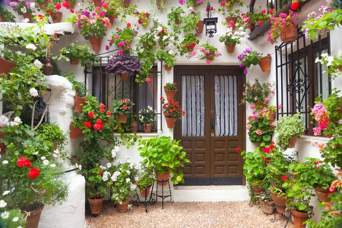 Un patio andaluz lleno de flores en macetas, con geranios rojos y rosas, ideal para inspirar tus ideas.