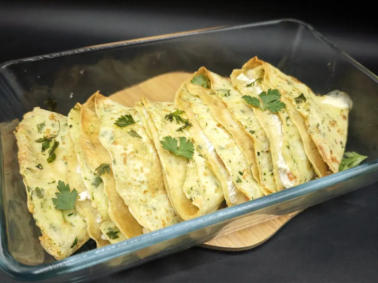 Deliziose crepes di zucchine ripiene, guarnite con prezzemolo fresco, pronte per essere gustate in una pirofila di vetro.