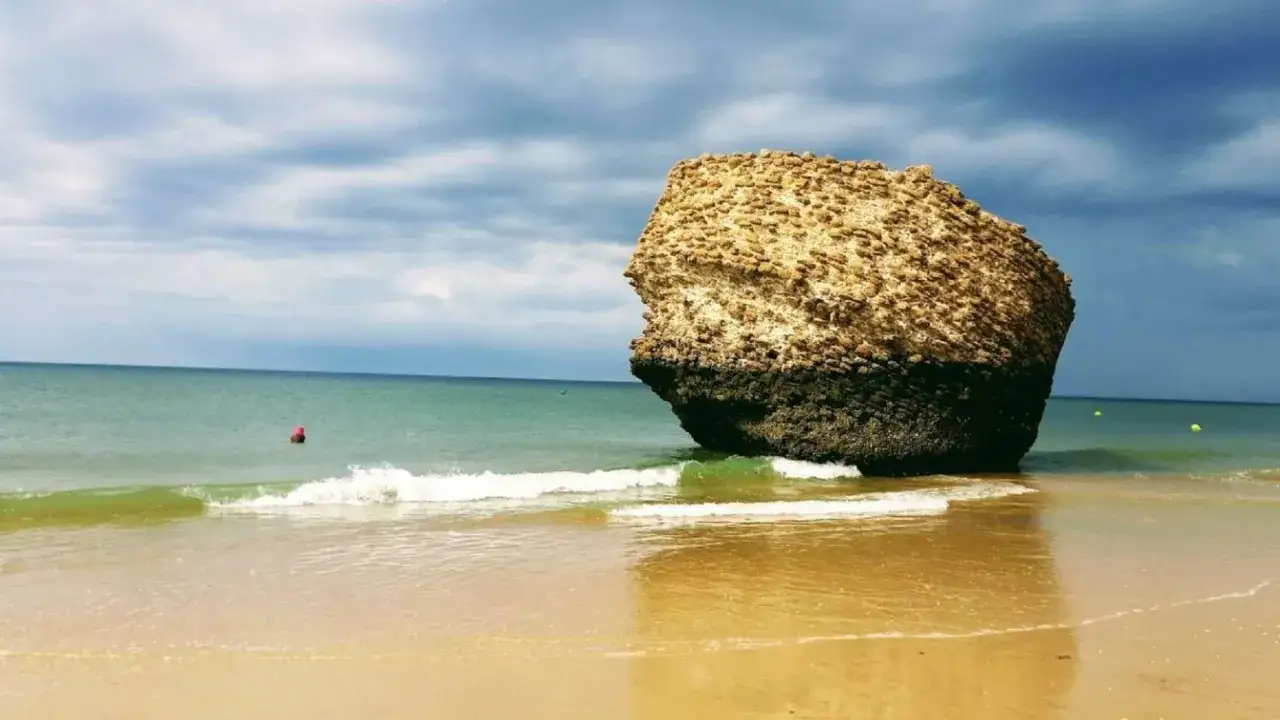 Felsformation am Strand der Costa de la Luz, mit sanften Wellen und einem dramatischen Himmel.