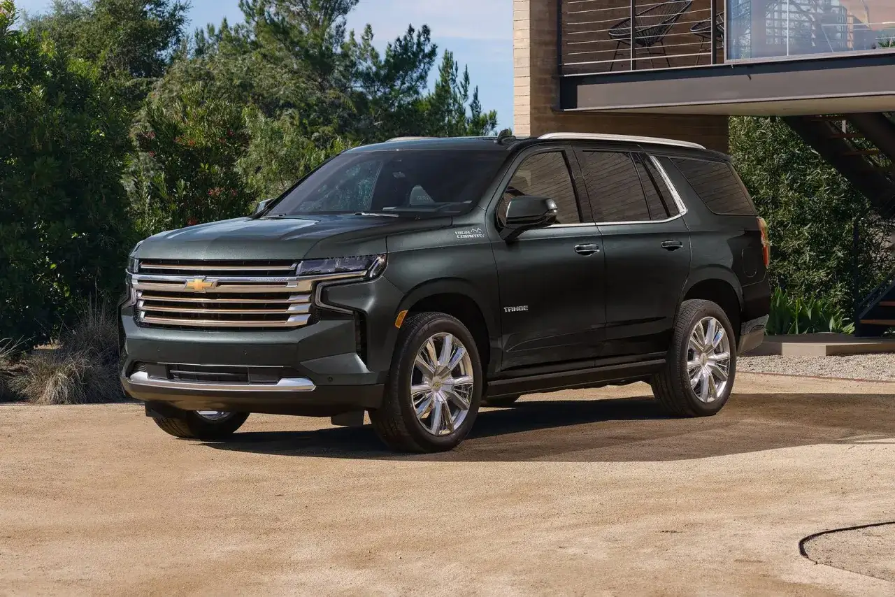Elegancki, ciemnozielony Chevrolet Tahoe High Country stoi przed nowoczesnym domem, gotowy na każdą przygodę.