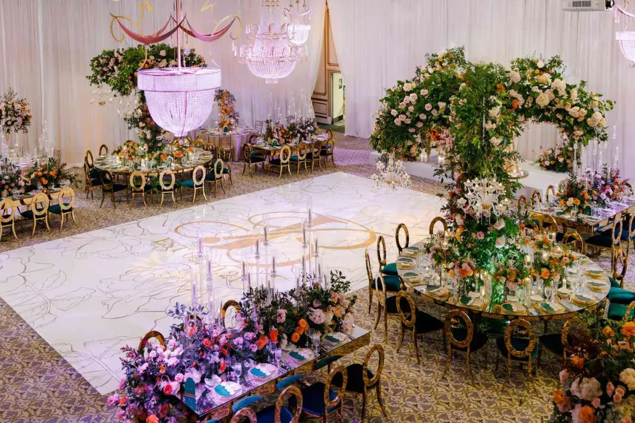 Elegancka sala weselna z kwiecistymi dekoracjami, kryształowymi żyrandolami i ozdobną podłogą. To idealne miejsce na niezapomniane atrakcje na wesele.