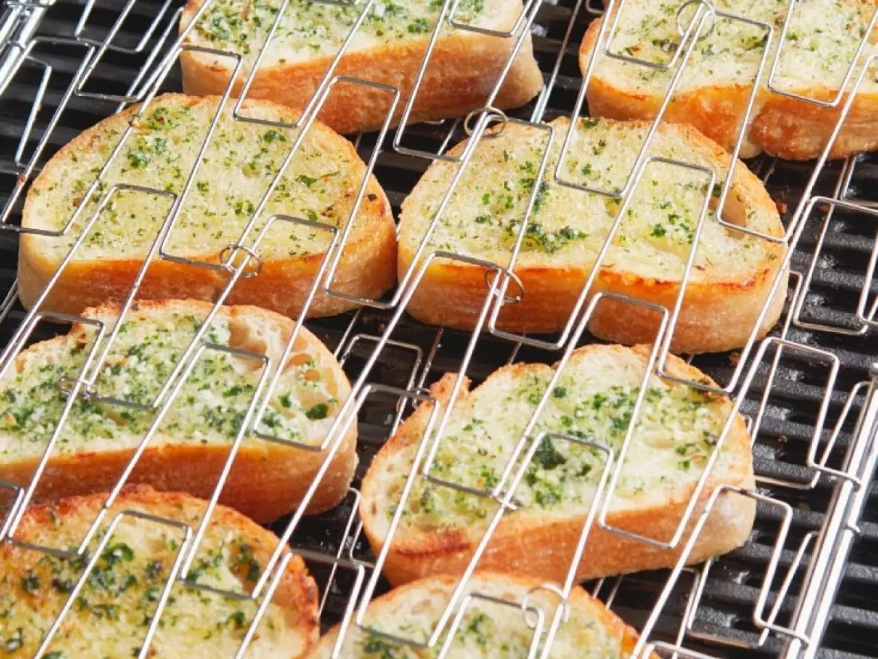 Knoblauchbutter selber machen: Ger&ouml;stete Brotscheiben mit Kr&auml;utern und Knoblauchbutter auf einem Grillrost.