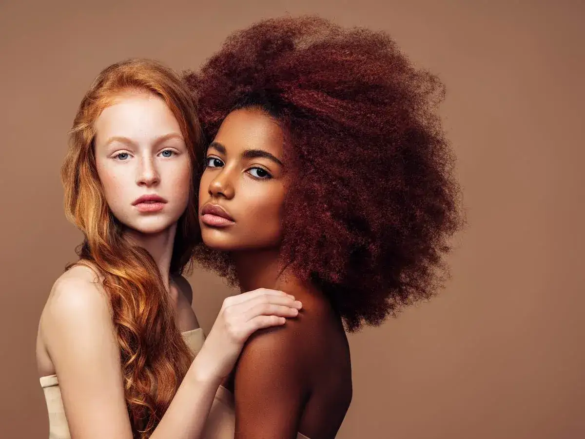 Deux jeunes femmes, l'une rousse et p&acirc;le, l'autre &agrave; la peau fonc&eacute;e et aux cheveux volumineux, se tiennent proches. Ces photos prises sur le vif capturent leur beaut&eacute; naturelle.