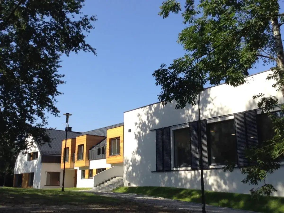 Nowoczesny dom dziecka z drewnianymi elementami i dużymi oknami, otoczony zielenią.