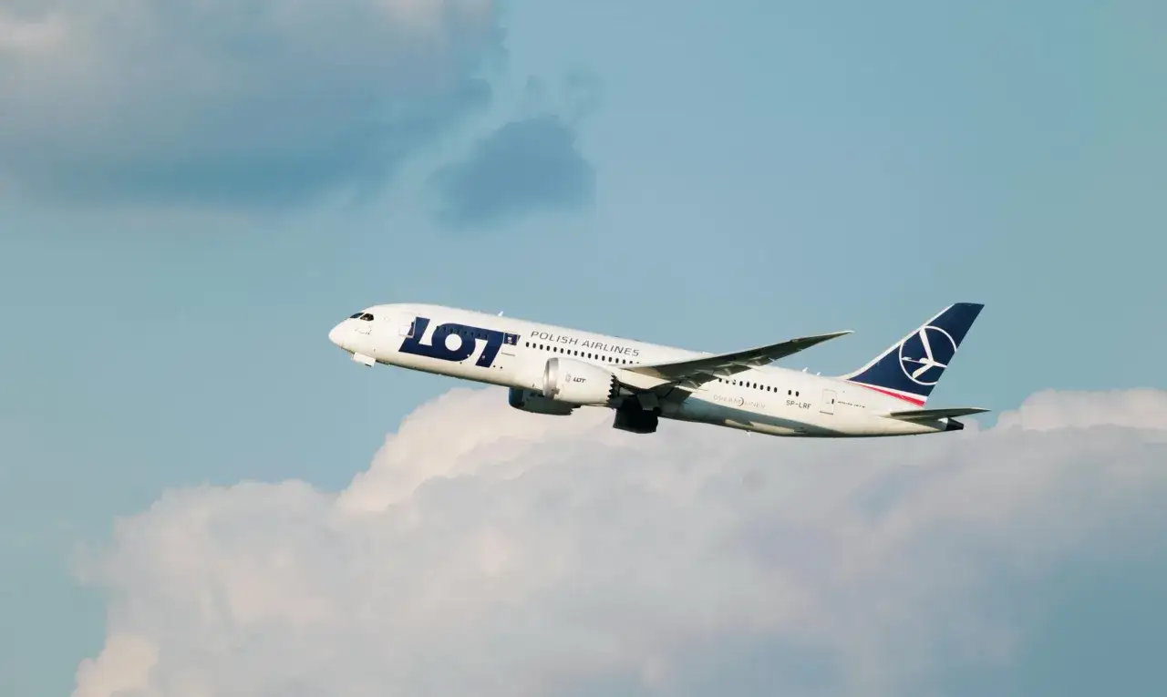 Samolot LOT Polish Airlines wznosi się na tle błękitnego nieba z chmurami.