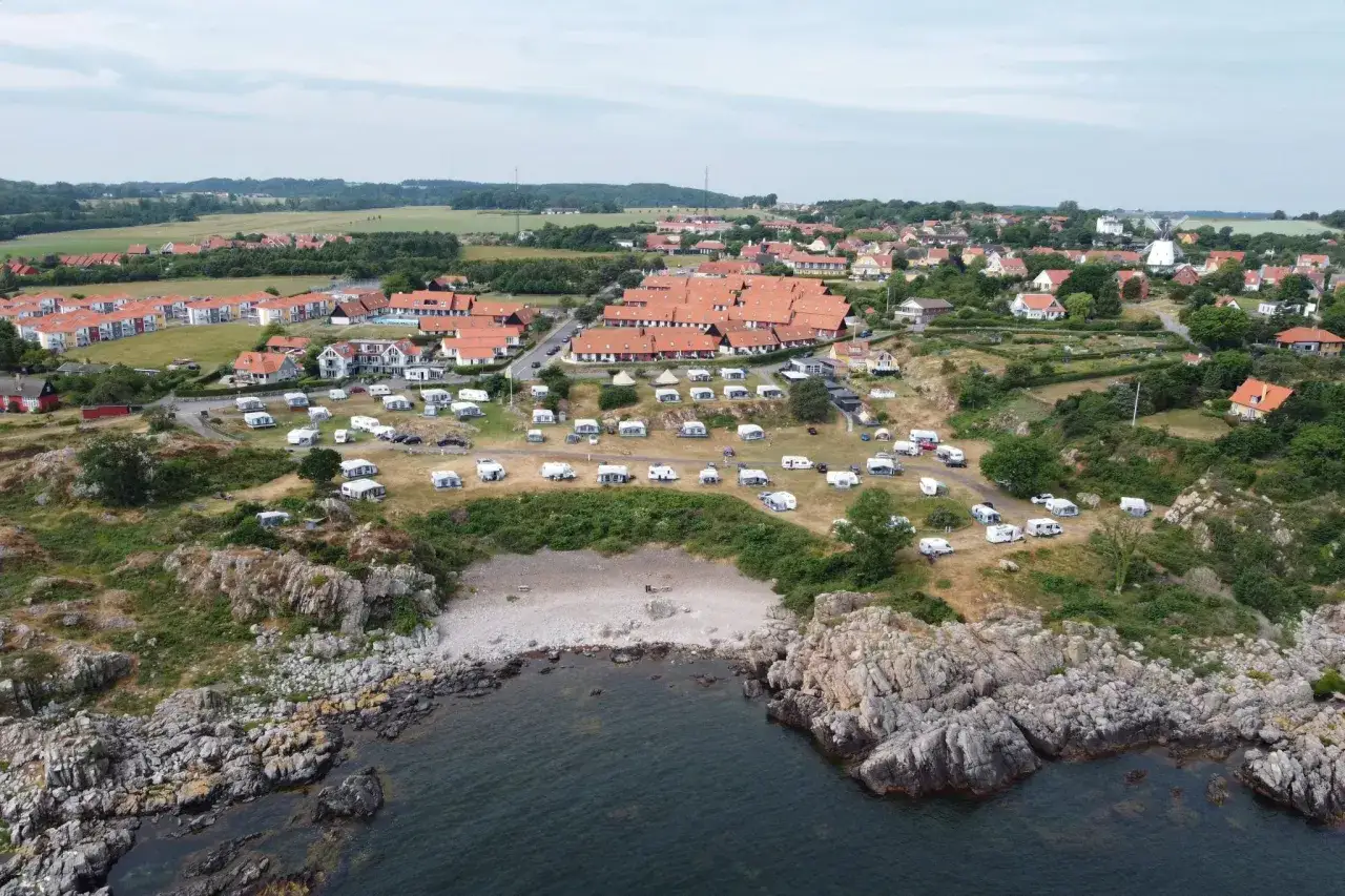 Sannes familjecamping vid kusten, med husvagnar och tält utspridda bland klippor och grönska.