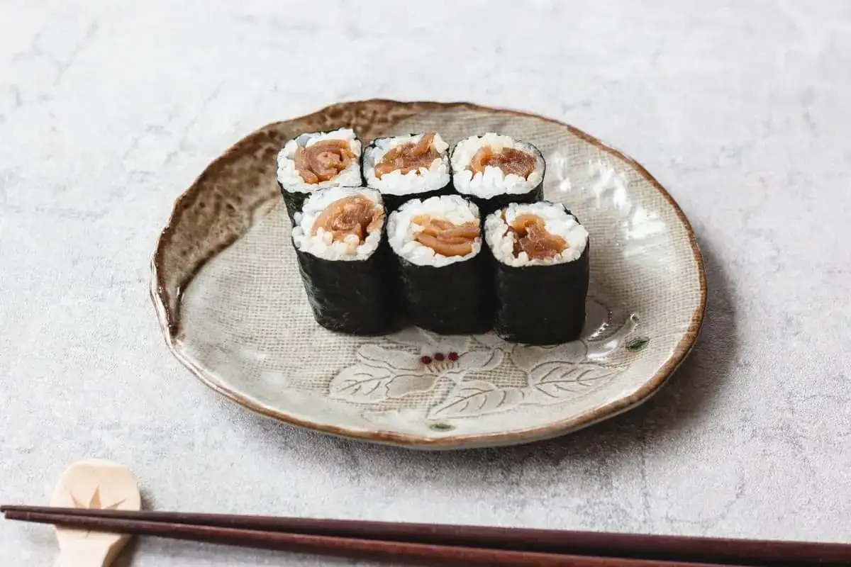 Sześć kawałków sushi z ryżem i farszem z tykwy, podanych na ozdobnym talerzu.