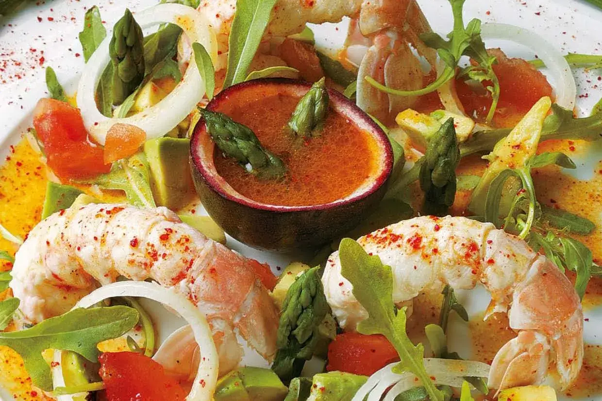 Salade de langoustines aux asperges, avocat, tomates et vinaigrette fruit&eacute;e, servie dans une demi-passiflore.