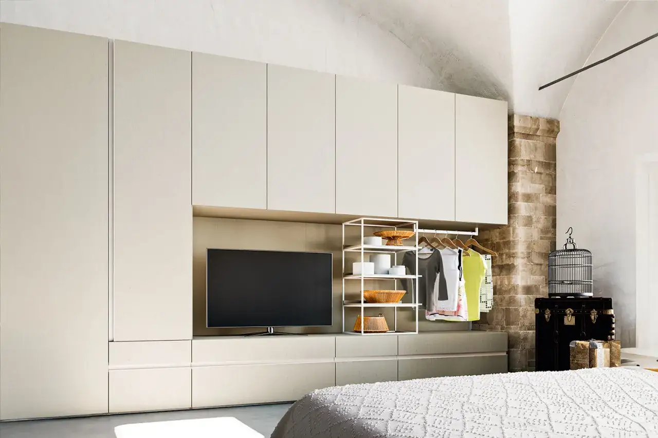Una moderna parete attrezzata con TV integrata, perfetta per la posizione tv camera da letto. C'è anche un armadio aperto con vestiti e una gabbia per uccelli decorativa.