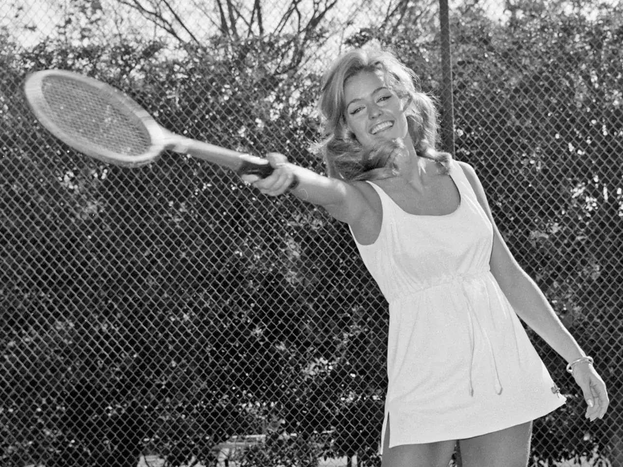 Una donna sorridente con un bracciale tennis colpisce una palla da tennis. La sua storia è legata a questo sport.