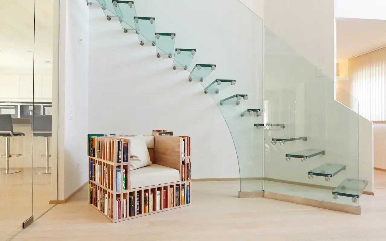 Escaleras de cristal modernas flotan en la pared, junto a un sill&oacute;n-librer&iacute;a lleno de libros.