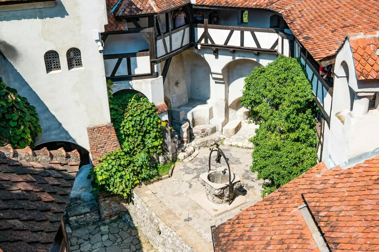 Dziedziniec zamku Bran w Rumunii z kamienną studnią i zielenią.