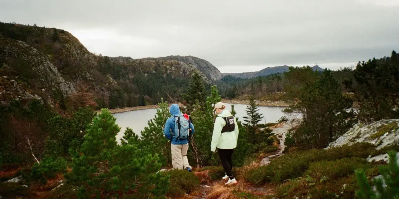 Två personer vandrar längs en stig med en sjö och berg i bakgrunden. En del av Sveriges vackra vandringsleder.