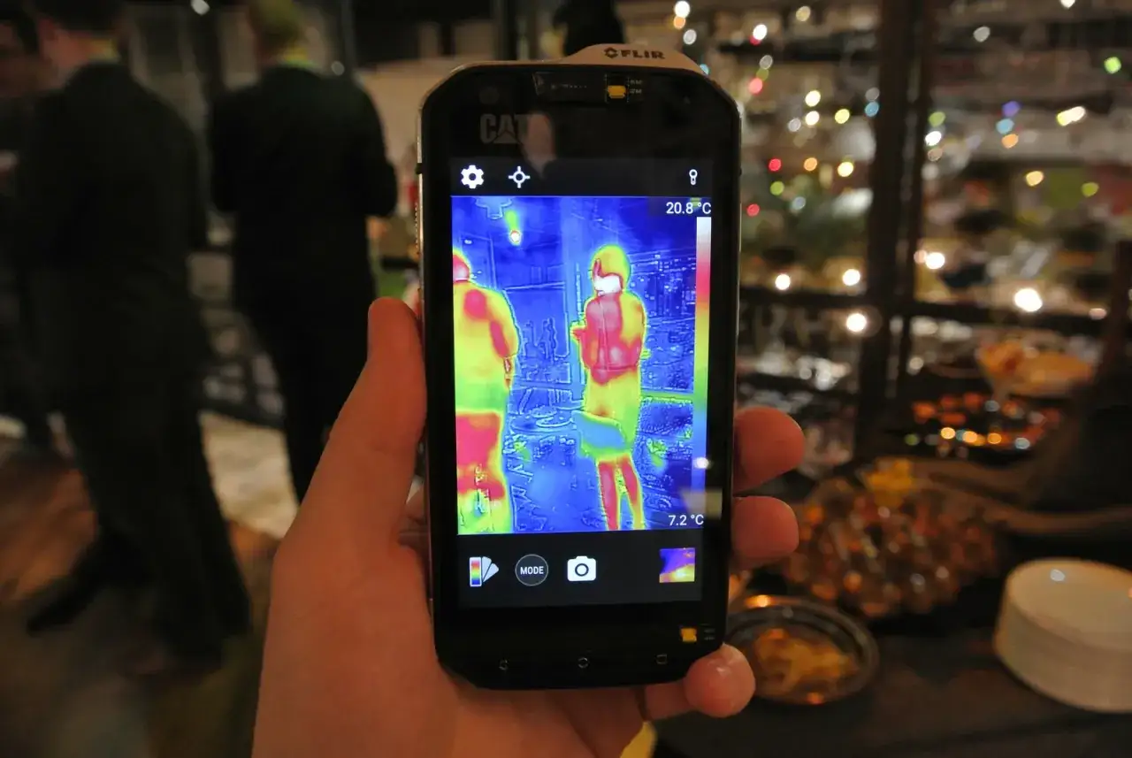 Dłoń trzyma smartfon Cat S60 z włączoną funkcją termowizji, pokazującą dwie osoby w cieplejszych barwach.