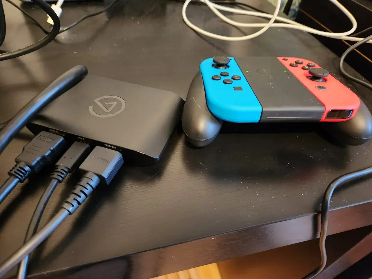 Chcesz wiedzieć, czy da się podłączyć Nintendo Switch do laptopa? Na zdjęciu widać sprzęt do przechwytywania obrazu, kable HDMI i USB-C, oraz kontrolery Joy-Con.
