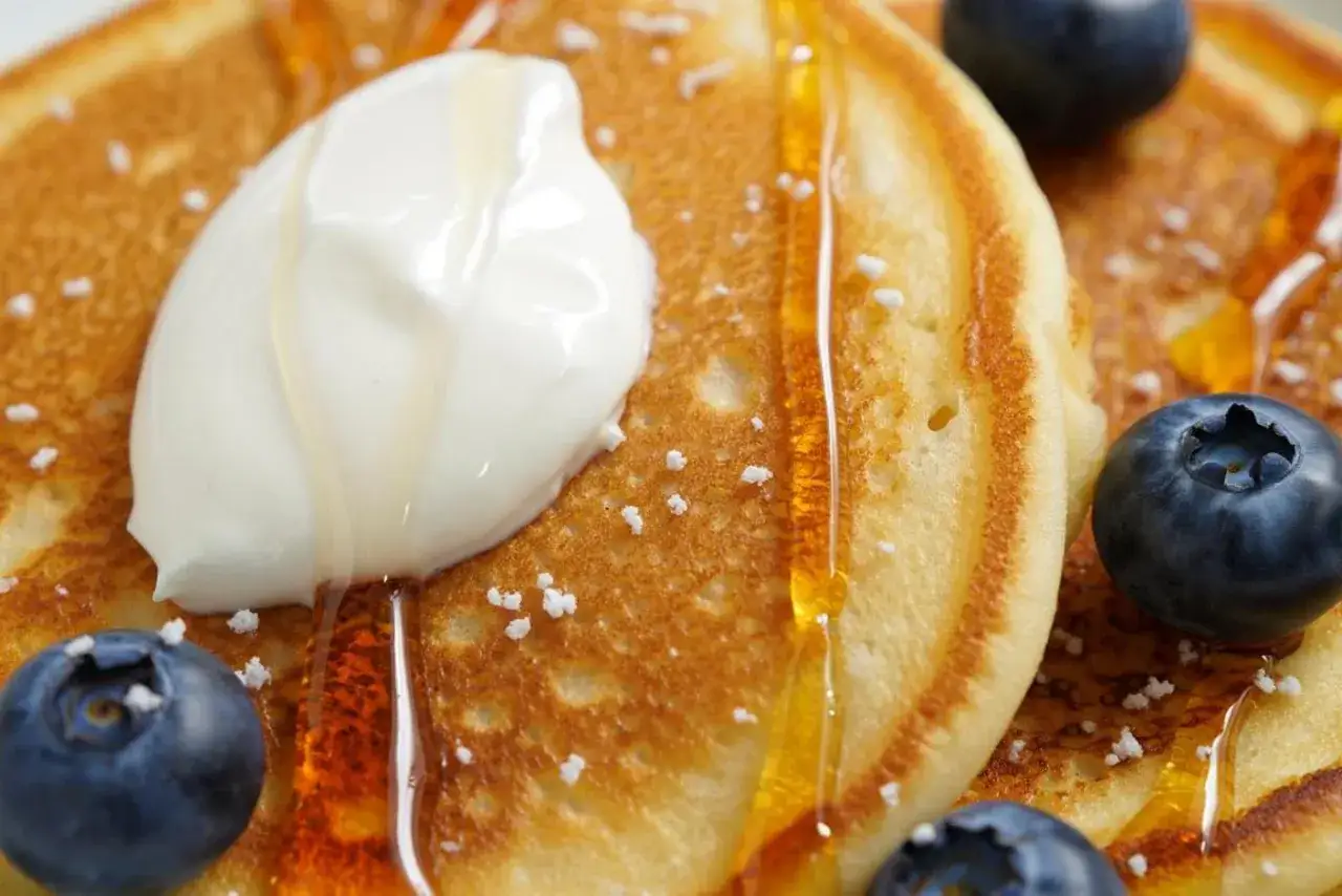 Fluffige Pancakes mit Kefir, garniert mit Honig, Blaubeeren und einem Klecks Sahne. Ein Genuss für jeden Morgen!