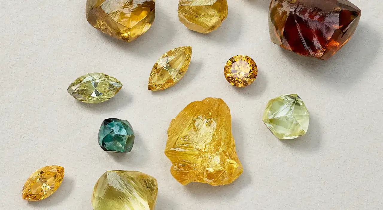 Una collezione di diamanti grezzi e tagliati, che mostrano un'affascinante gamma di colore diamanti: dal giallo intenso al verde acqua, fino al rosso ambrato.