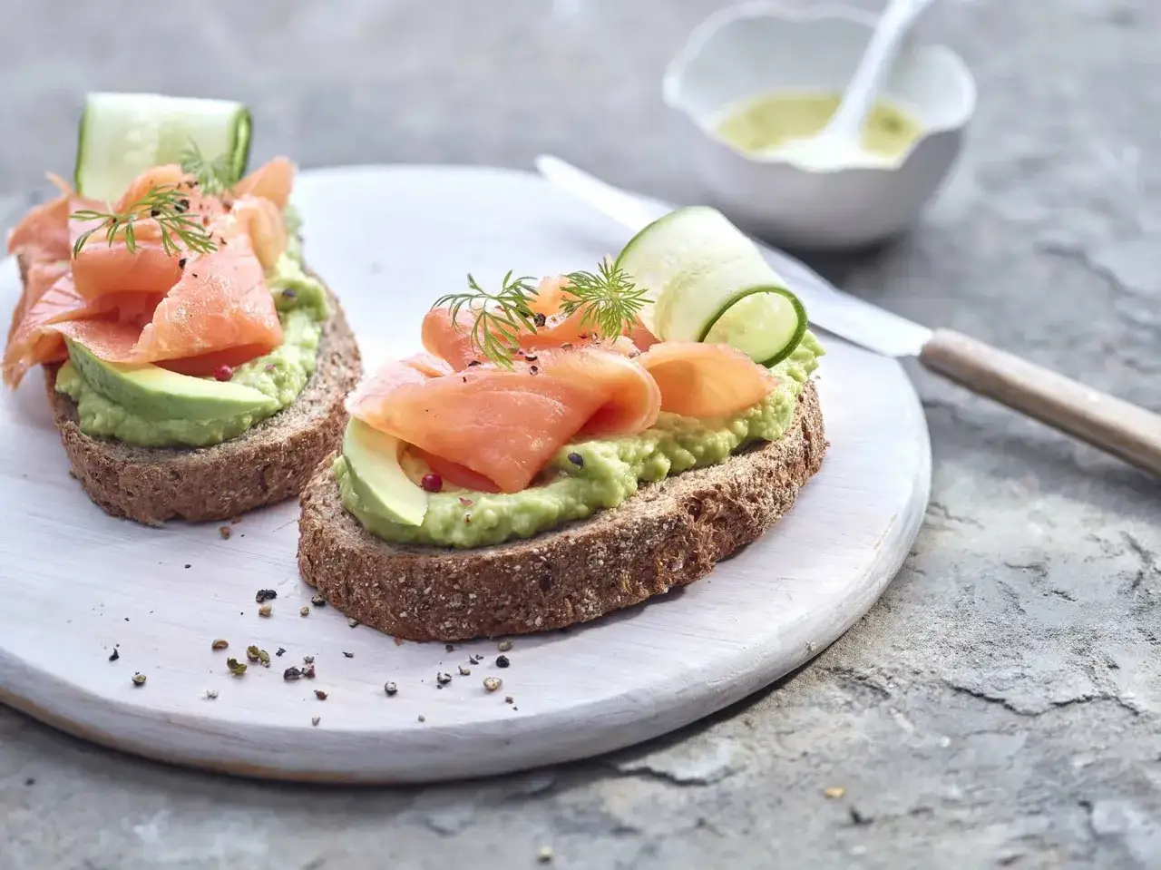 Deux toasts avocat saumon, garni de concombre et d'aneth, sur un plateau blanc.