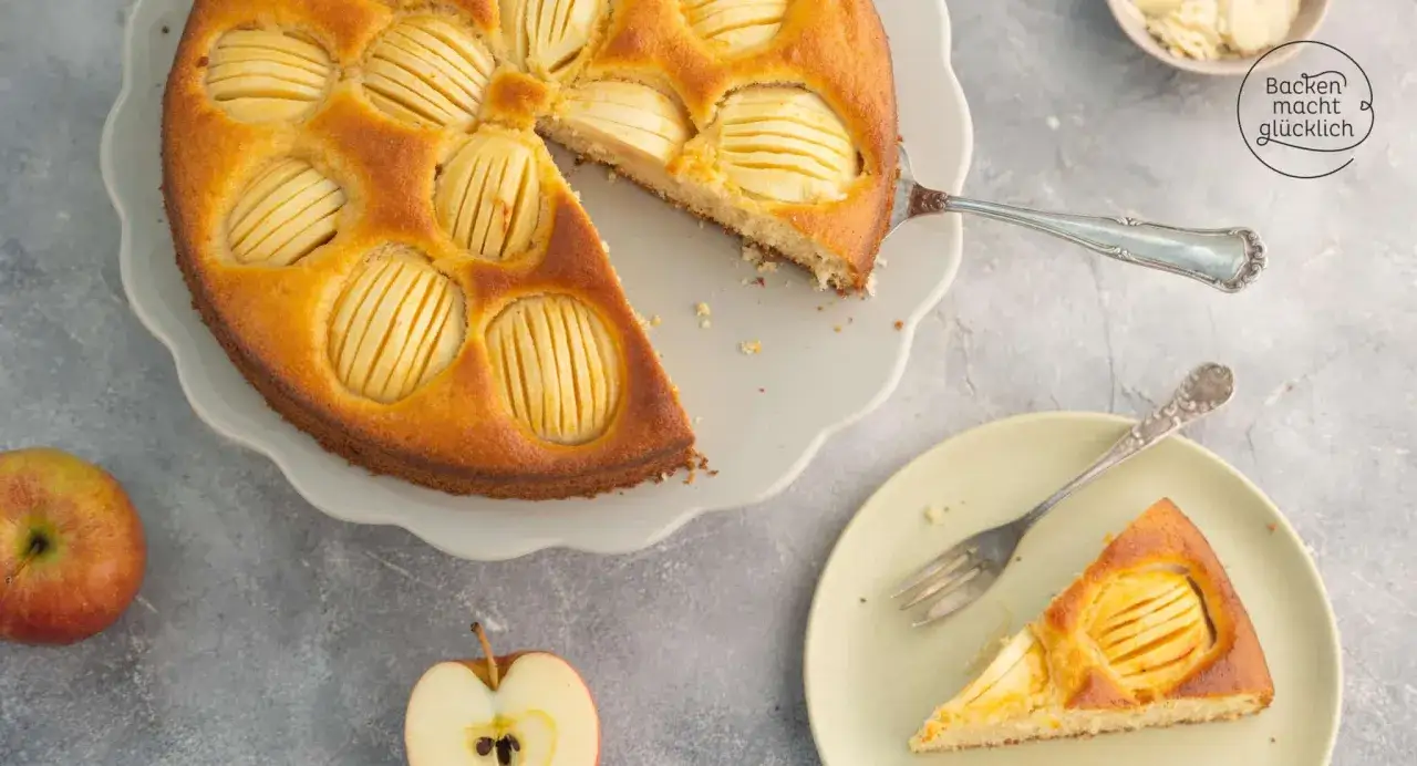 Ein goldbrauner Apfelkuchen mit vielen Apfelscheiben, der Lust auf tolle Apfelkuchen Rezepte macht. Ein St&uuml;ck ist bereits auf einem Teller angerichtet.