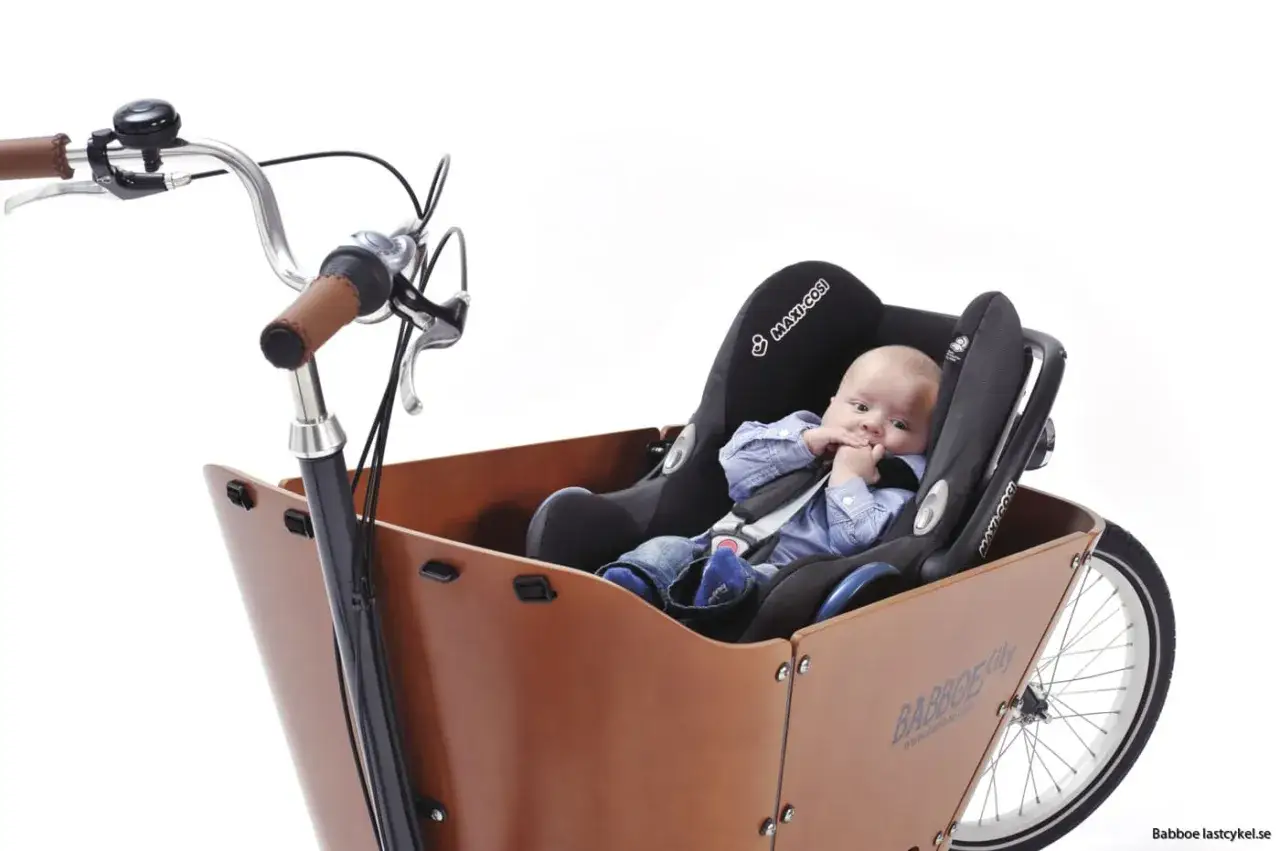 Säker cykeltur med bebis i cykelkorg. En liten bebis sitter tryggt i en bilbarnstol monterad i en lastcykel.