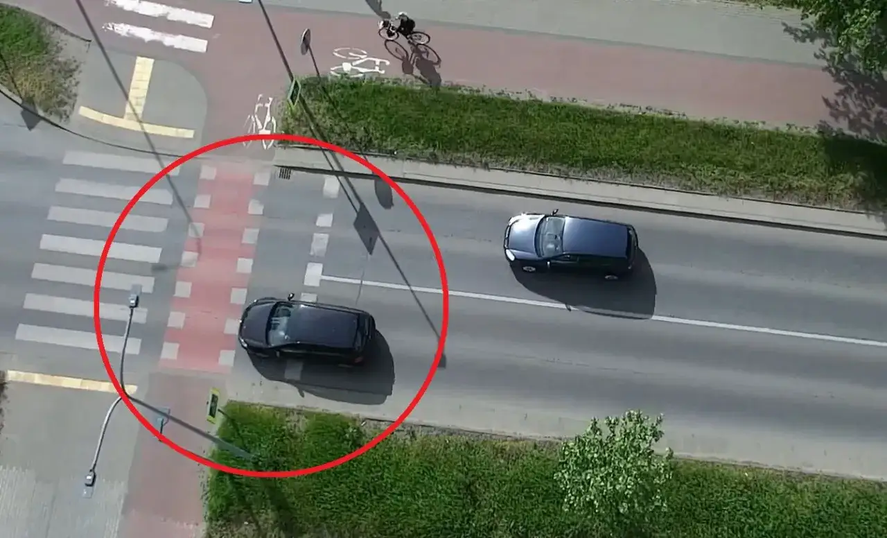 Niebezpieczne wyprzedzanie na pasach. Czarny samochód omija stojący pojazd, ryzykując potrącenie pieszego.