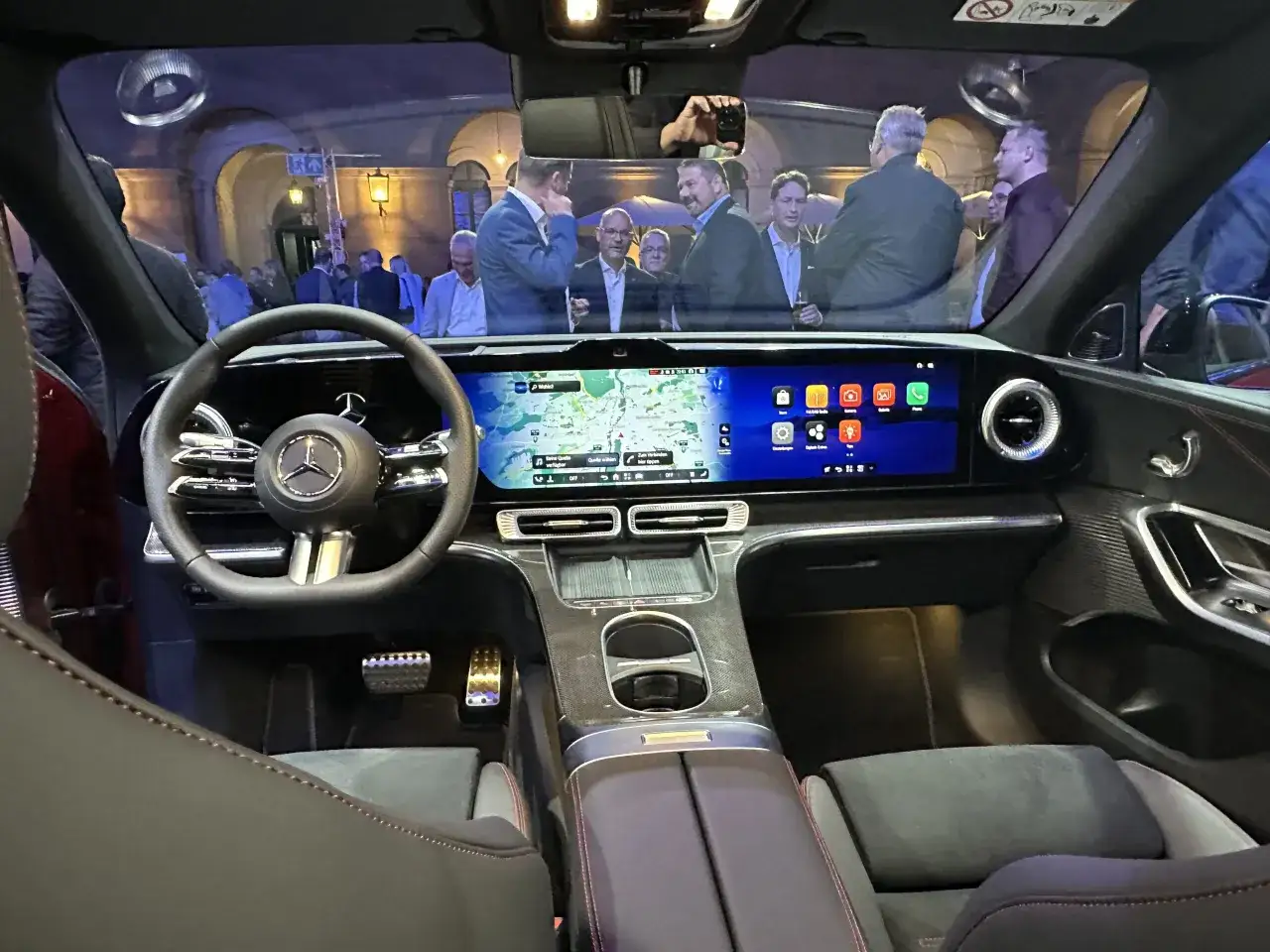 Innenansicht eines Mercedes GLC EQ mit Navigationssystem und Infotainment. Personen stehen im Hintergrund.