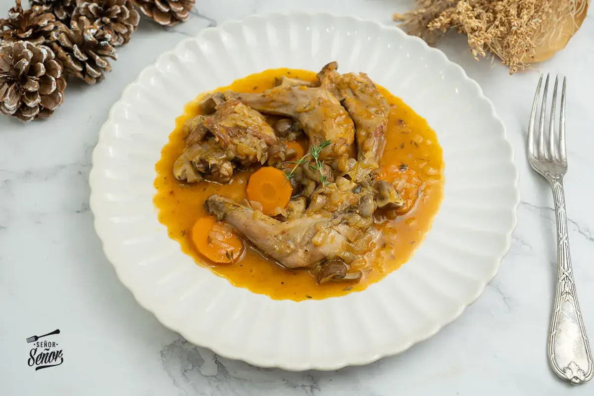 Delicioso conejo a la cazadora en salsa con zanahorias y champiñones, servido en plato blanco con tenedor.