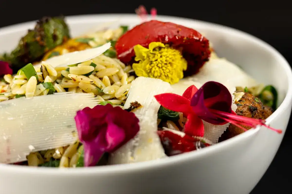 Eleganckie metody serwowania potraw: makaron orzo z parmezanem, pomidorem, ziołami i jadalnymi kwiatami w białej misce.