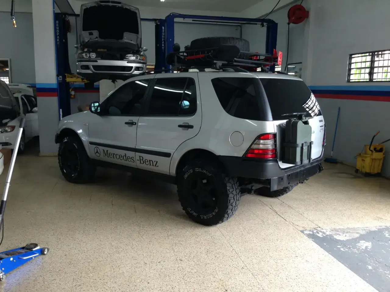 Srebrny Mercedes ML 320 z bagażnikiem dachowym i terenowymi oponami, gotowy na przygodę.