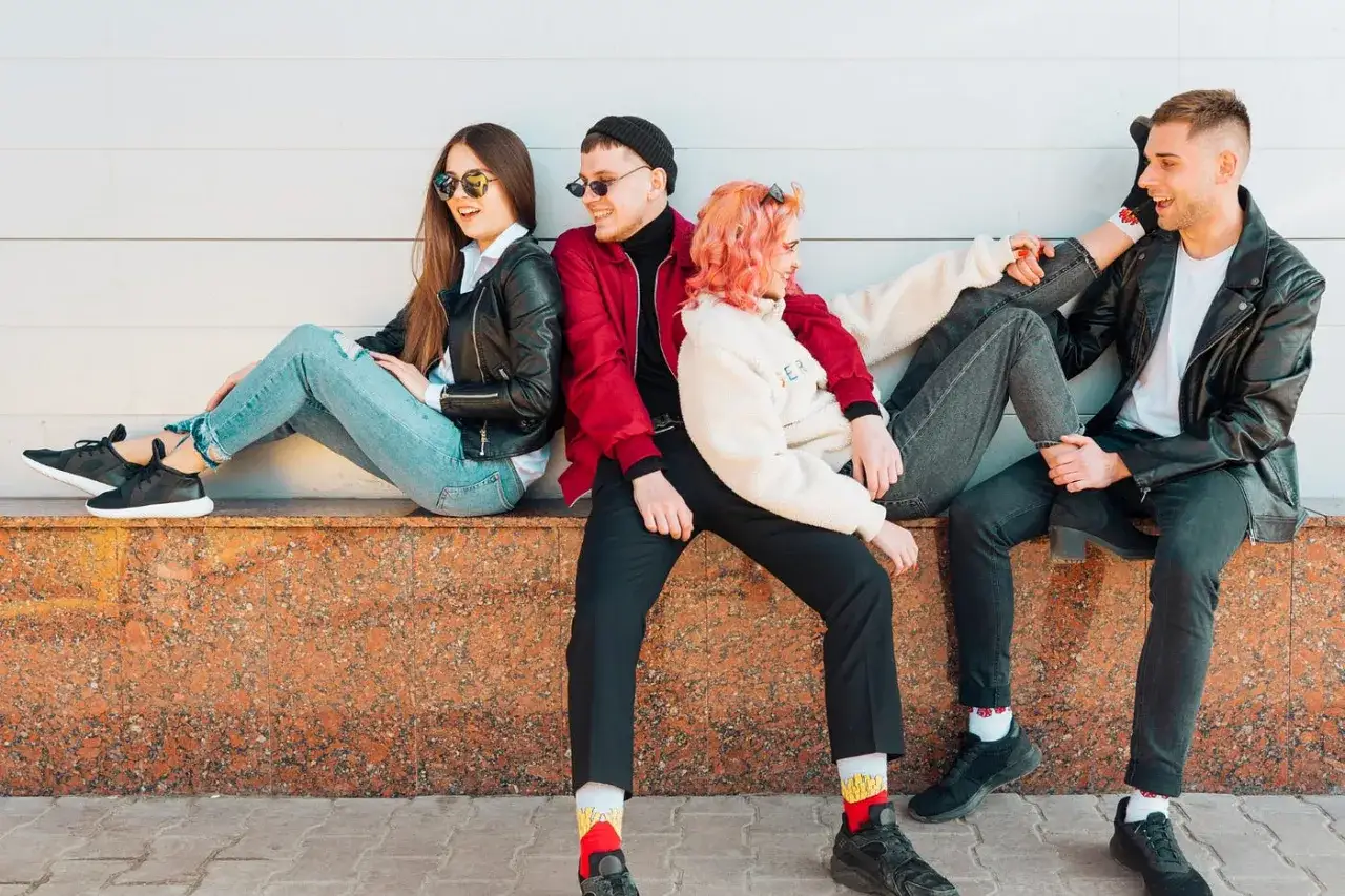 Młodzież prezentuje różne style ubioru: skórzane kurtki, jeansy, kolorowe bluzy i modne skarpetki.