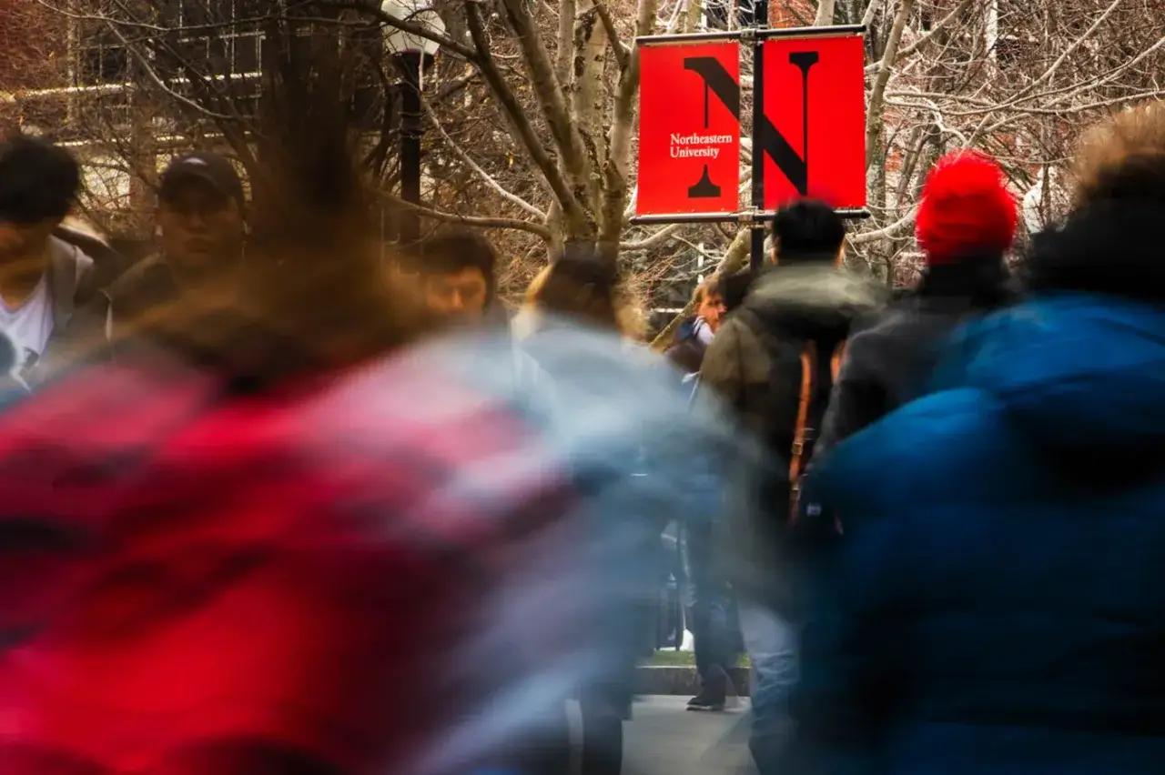 Students rush past a Northeastern MPA banner on a chilly day.