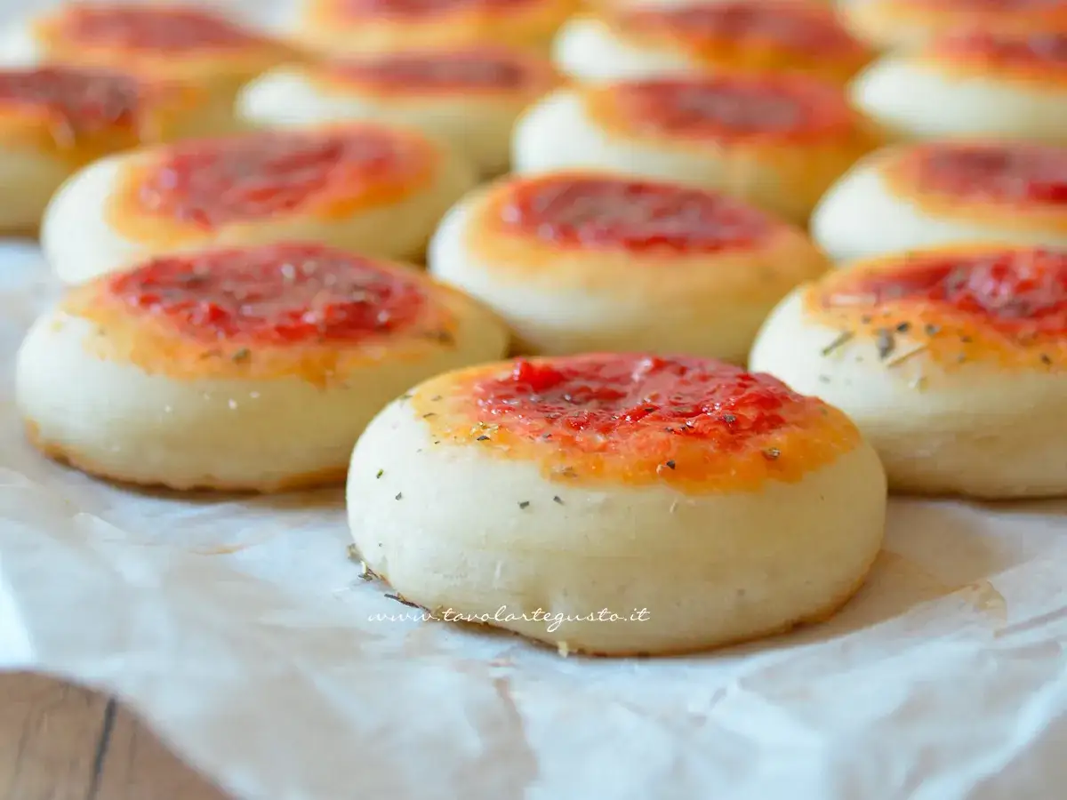 Pizzette fatte in casa, piccole e invitanti, con un soffice impasto e un tocco di pomodoro e erbe aromatiche.